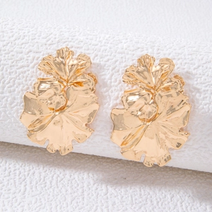 Macro view of gold flower earrings with detailed hammered texture on white stone pedestal