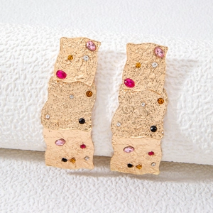 Close-up of golden flower earrings with hammered texture and multicolored rhinestones