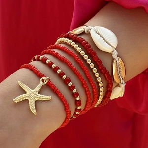 Detalle de pulseras bohemias de cuentas rojas y dijes de concha en la muñeca