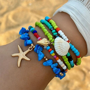 Primer plano de tobilleras bohemias con cuentas y dijes de estrella de mar en la playa