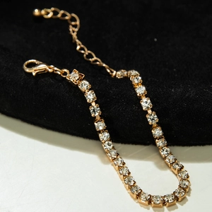 Detailed close-up of a golden tennis bracelet with square-cut crystals on a velvet stand