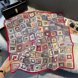 Detail of color-block geometric square silk scarf draped on soft white plush surface