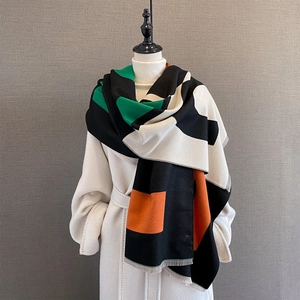 Detailed view of geometric color-block scarf with tassel edges on a beige wool coat