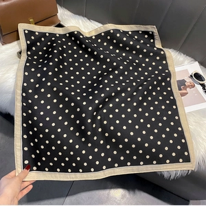 Close-up of elegant black polka dot square scarf draped on a white faux fur texture