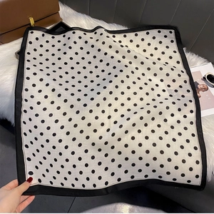 Detail of square polka dot silk scarf with black border on a white plush background