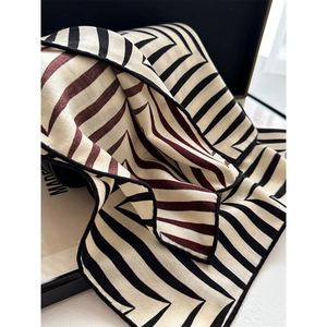 Silk blend scarf with geometric stripes in black and tan draped over a gift box