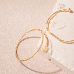 Minimalist gold chain and spiral bangles displayed on natural stone texture background