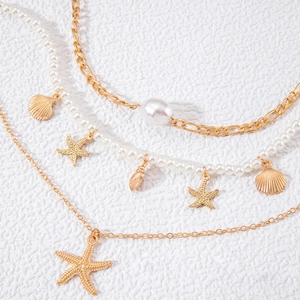 Detail of multilayer gold chain necklace with faux pearls and starfish shell charms