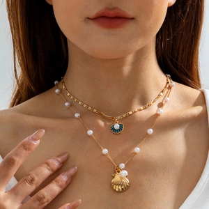 Close-up of layered necklace with gold scallop shell charms and pearls on model neck
