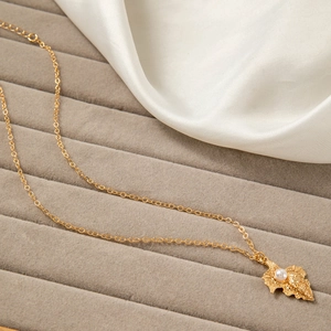 Detail of gold necklace with seashell pendant, pearl inlay on soft satin fabric