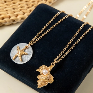 Detailed close-up of golden starfish and conch pendants with pearls on blue velvet