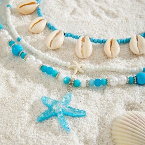 Detail of bohemian shell necklace set with blue starfish pendant on white sand beach