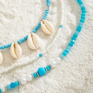 Macro detail of Bohemian shell necklace with blue beads and pearls on white sand