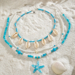Detail of bohemian layered necklace set with blue beads, sea shells and starfish on sand