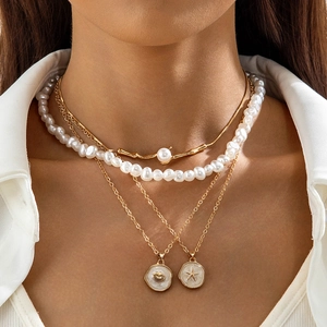 Detail of layered gold necklaces with faux pearls, seashell and starfish charms on a white shirt