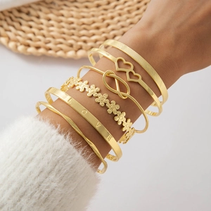 Detail of gold bracelet set with LOVE engraving and heart charms on model wrist