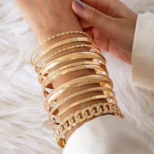 Close-up of stacked gold-plated bracelets including arrow patterns and chunky chain links