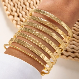 Set of 7 gold-toned textured bangles including hammered and star patterns on model wrist