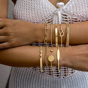 Close-up of layered gold bracelets with geometric patterns and braided textures on model