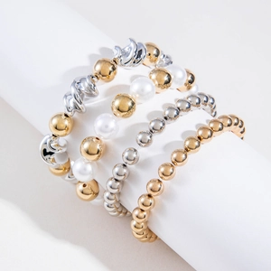 Détail de bracelets superposés en perles dorées et argentées avec perles blanches