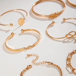 Macro detail of gold-plated open bangles and chunky chain bracelets with twist patterns