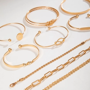 Close-up of gold layered bracelet set featuring chunky chains and twisted open bangles
