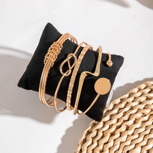 Detail view of five-piece gold bangle set with braided and geometric patterns on a cushion