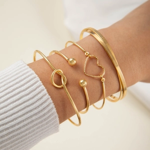 Detailed view of 5-piece gold bangle set with heart charm on white knit sweater sleeve