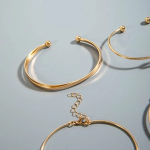 Detailed view of gold bangle set featuring polished sphere ends and adjustable chain clasp