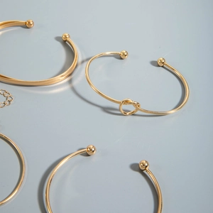Detail view of gold-plated bracelets featuring minimalist rods and twisted knot designs