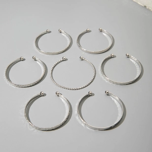 Detailed view of seven silver open bangles with diverse textured patterns and bead ends