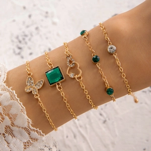 Dettaglio del set di 5 bracciali dorati con cuore di smeraldo e farfalla sul polso