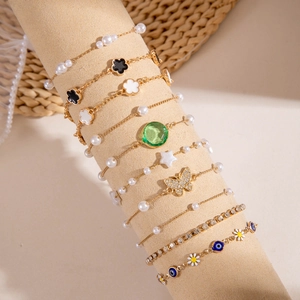 Dettaglio del set di bracciali dorati con finti smeraldi, perle e vari motivi floreali