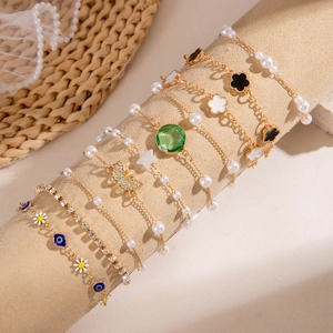 Dettaglio di bracciali dorati con cuori di smeraldo, perle e set di ciondoli a farfalla