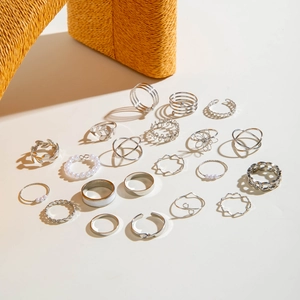 Detailansicht eines silbernen Stapelring-Sets mit Blatt- und Perlendesign auf Beige