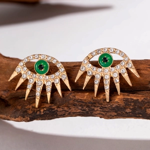 Detail of gold hollow eye earring with green stone, white rhinestones, and long lashes