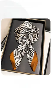 Gros plan d'un foulard en soie zébré avec bordure orange dans une boîte cadeau noire