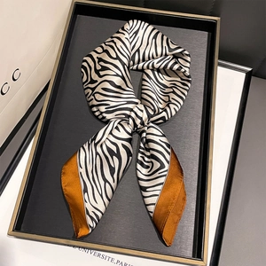 Carré de soie chic avec motif zébré et bordure orange disposé sur un plateau noir