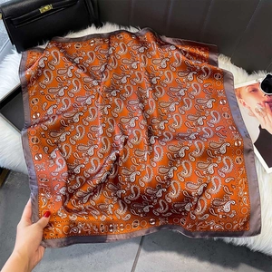 Detail of orange paisley silk square scarf with brown border and smooth satin texture