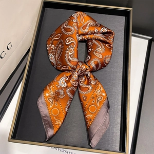 Detail of orange paisley silk scarf with sun patterns tied in a bow on a display tray