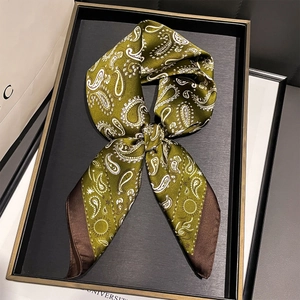 Detail view of a green paisley silk scarf folded into a bow on a black decorative tray