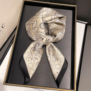 Close-up of champagne gold paisley silk scarf with black borders on a luxury tray