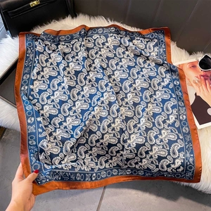 Detail of paisley print silk scarf laid on white fur with sunglasses and a handbag