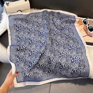 Close-up of a navy paisley silk scarf styled with a white bag and sunglasses