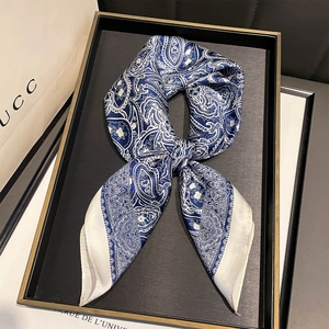 Detail of navy paisley silk scarf tied in a bow on a tray with luxury background