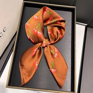 Détail d'un foulard en soie marron avec motif cerises noué en boucle sur un plateau noir