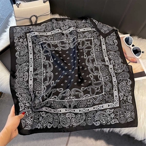 Elegant black and white paisley print square silk scarf on a plush white decorative surface
