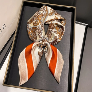Close-up of silk-textured orange paisley and striped square scarf in a luxury tray