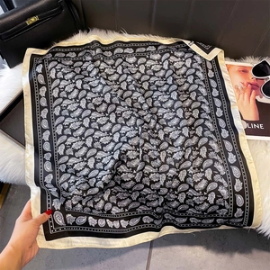 Detail of paisley print silk scarf with beige border laid on a plush background