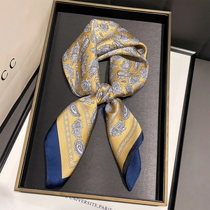 Detail of yellow and navy paisley silk-like square scarf tied in a bow on a black tray
